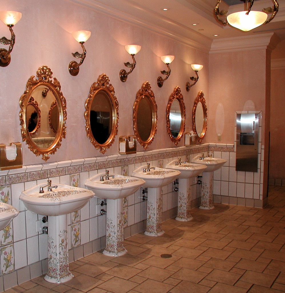 Ornate resort restroom with gold-framed mirrors and floral pedestal sinks